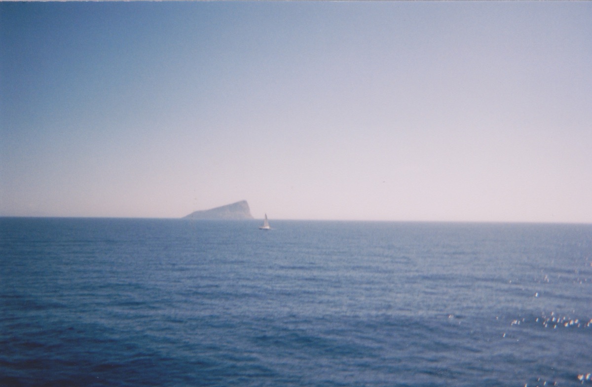 A sailboat passing a distant headland on a calm sea